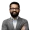 Professional head and shoulders portrait of a man with a beard and glasses wearing a gray blazer and striped shirt arms crossed