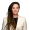 Professional head and shoulders portrait of a woman with long brown dreadlocks wearing a beige blazer over a dark top looking at the camera