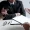 Two professionals shake hands across a desk with a clipboard of papers glasses and a pen nearby