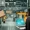 The Shifting Equation The Portfolio Factory floor with yellow robotic arms passing a cardboard box to a worker holding a laptop displaying blueprintsschematics