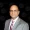 Yad Senapathy1200800 The Portfolio Professional head and shoulders portrait of a man in a gray suit white shirt and red blue plaid tie against a dark background with portfolio watermark